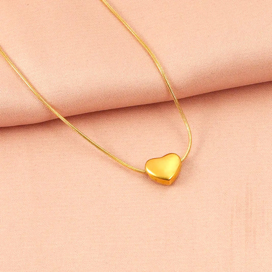 Gold heart pendant necklace resting on a soft peach fabric background.