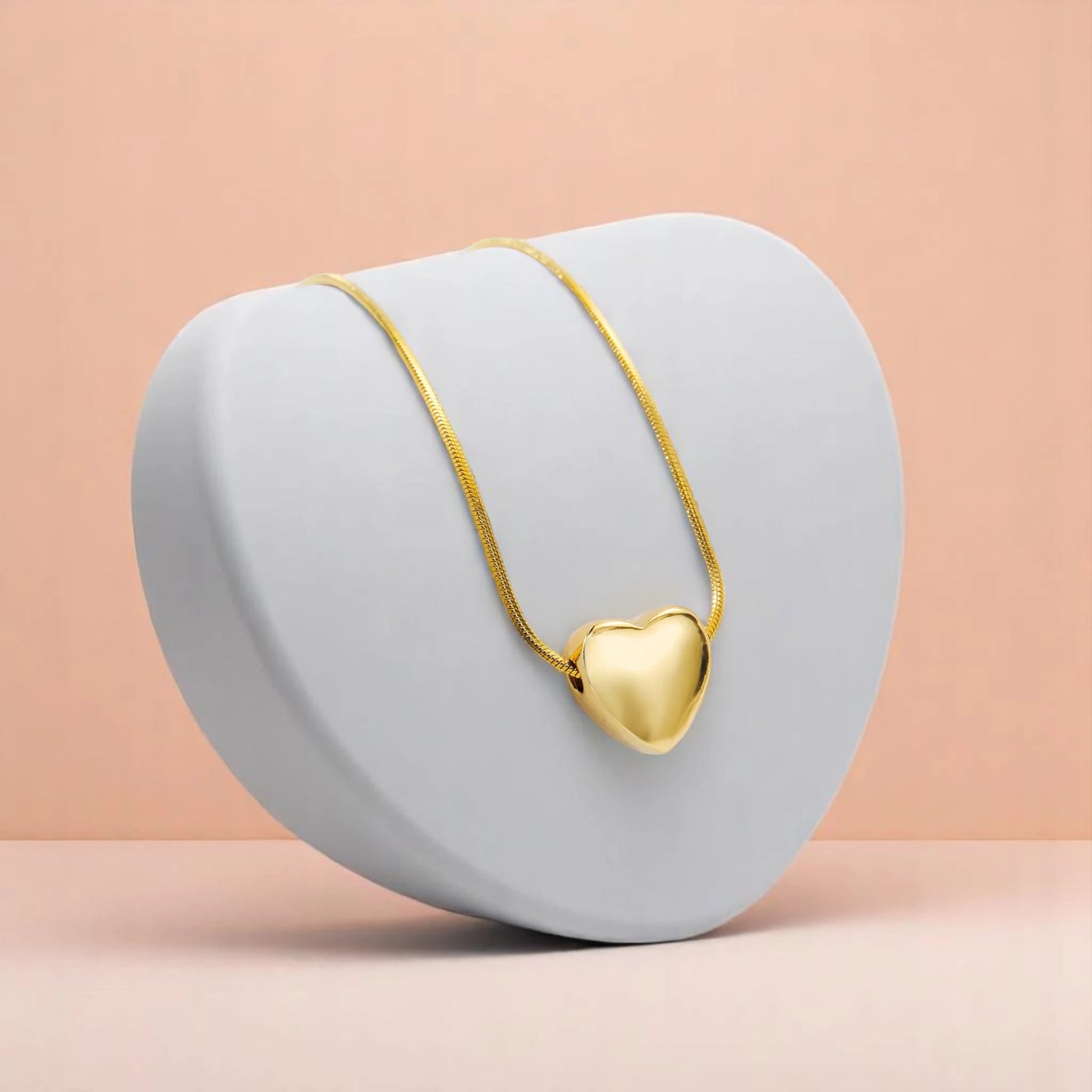 Necklace displayed on a smooth, gray, heart-shaped stand against a soft peach background.