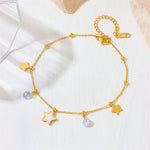 A gold chain bracelet with star and moon charms, displayed on a light textured background. The bracelet features three gold star charms, one light blue crystal bead, and one white crystal bead, with a gold clasp and extender chain.