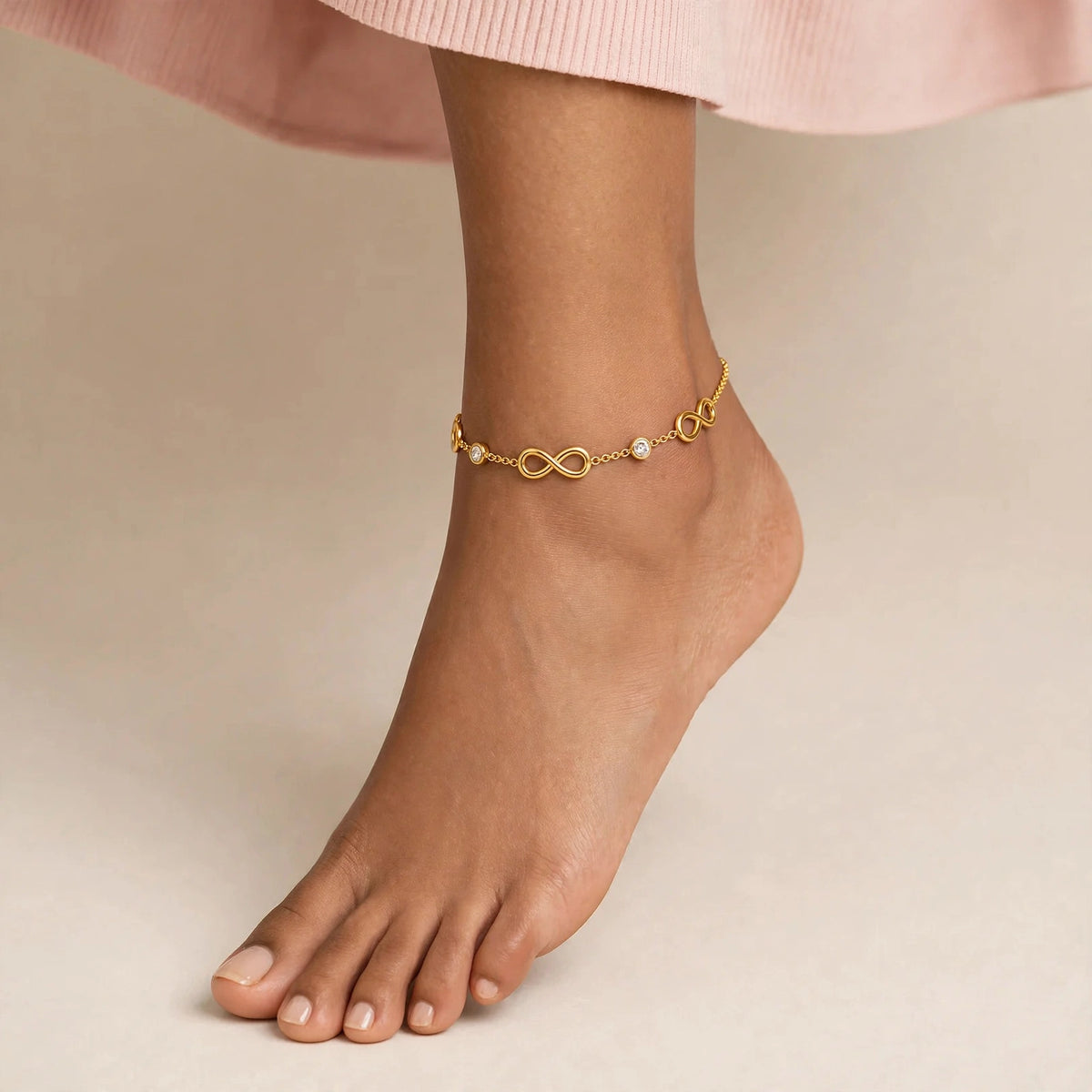 Indian woman foot pointed wearing gold infinity anklet with CZ stones, blush top.