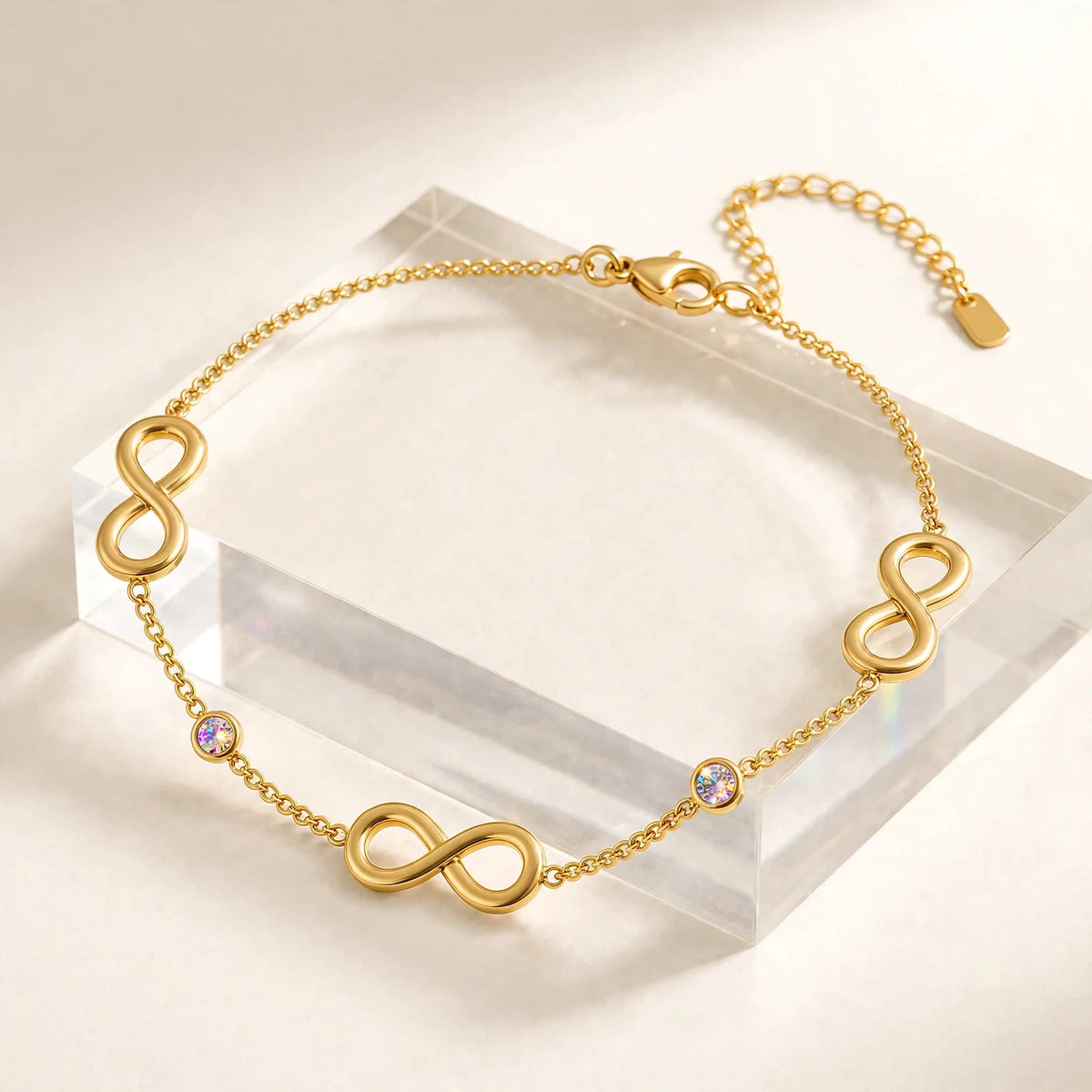 Side profile of gold infinity anklet showing thickness and dimension on clear riser.