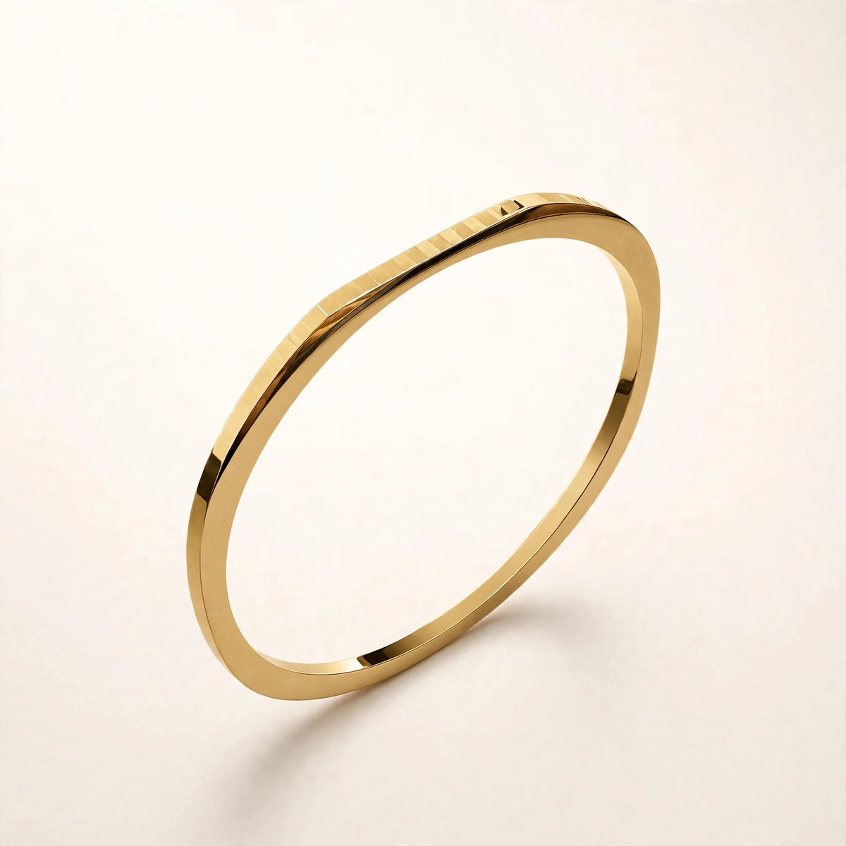 Thin gold faceted bangle floating at angle on off-white background, mirror-polished.
