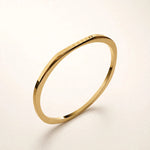 Thin gold faceted bangle floating at angle on off-white background, mirror-polished.