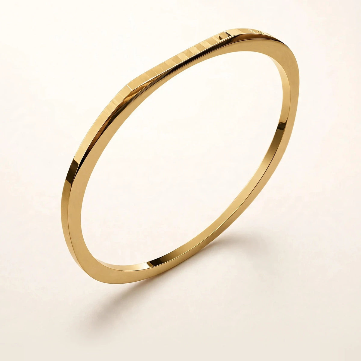 Thin gold faceted bangle floating at angle on off-white background, mirror-polished.
