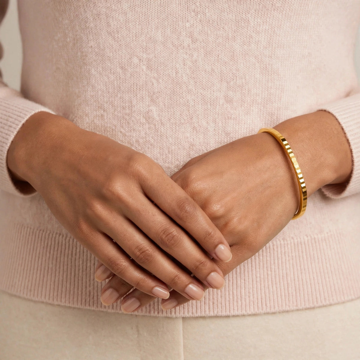 Indian woman hands at waist wearing thin gold bangle with flat edges, blush sweater.