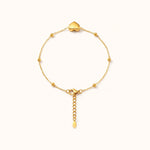 Gold puffy heart bracelet with beaded ball chain on warm white, top-down circle view.
