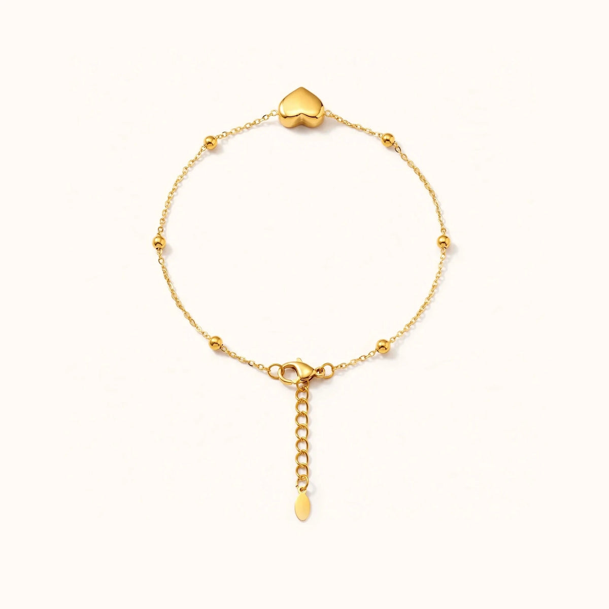 Gold puffy heart bracelet with beaded ball chain on warm white, top-down circle view.