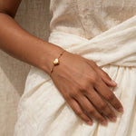 Indian woman in ivory top forearm across waist showing gold heart bracelet
