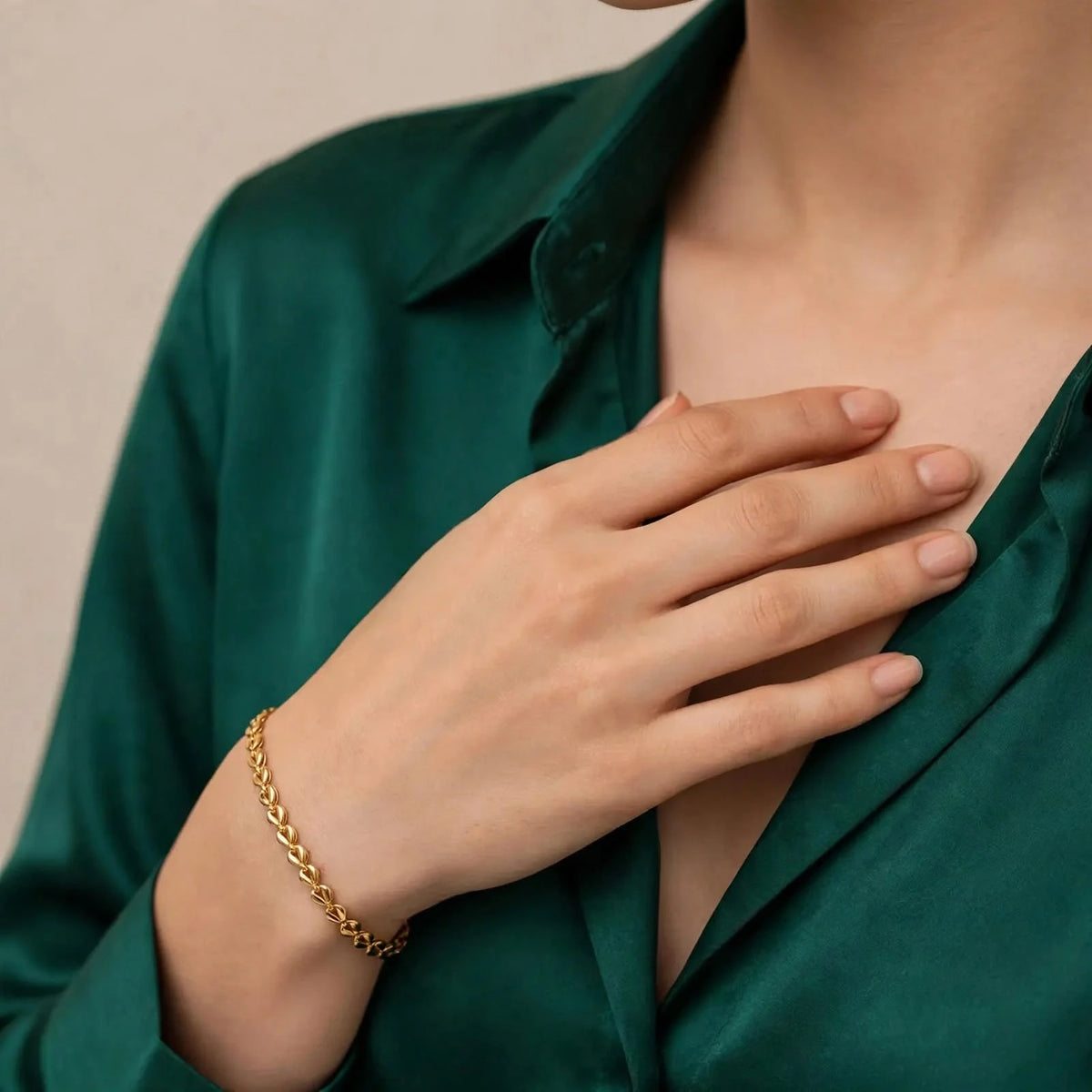 Gold teardrop chain bracelet on a fair-skinned hand against an emerald green silk open-collar top.
