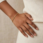 Hand on hip with gold teardrop chain bracelet, ivory fine-knit sweater close-up.