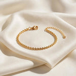 Gold teardrop chain bracelet on ivory silk fold, side light and shadow.