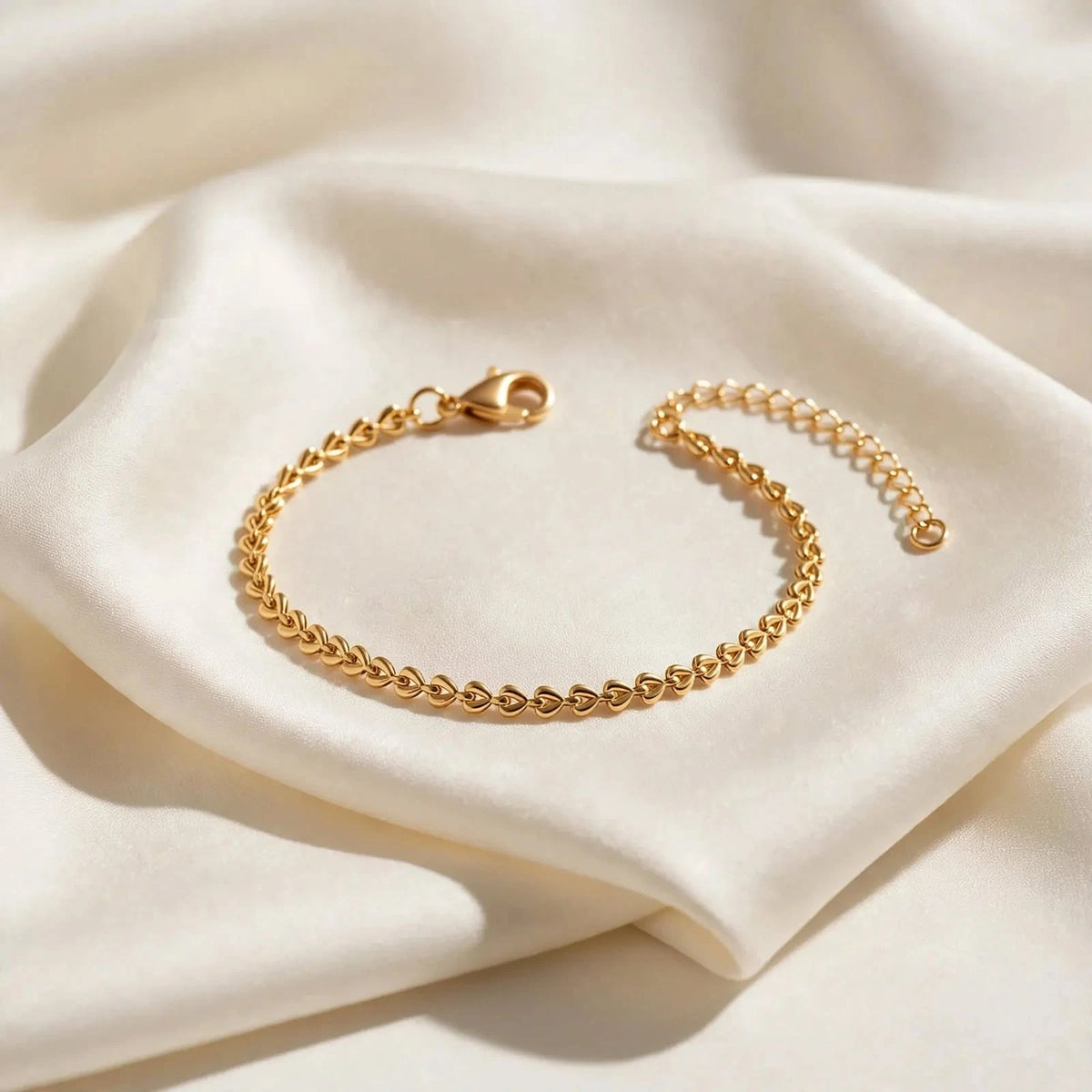 Gold teardrop chain bracelet on ivory silk fold, side light and shadow.