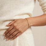 Woman's wrist with gold box chain bracelet, ivory knit sweater, soft neutral backdrop