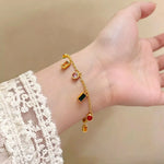 Gold charm bracelet with colorful gemstone charms on woman's wrist with white lace sleeve.