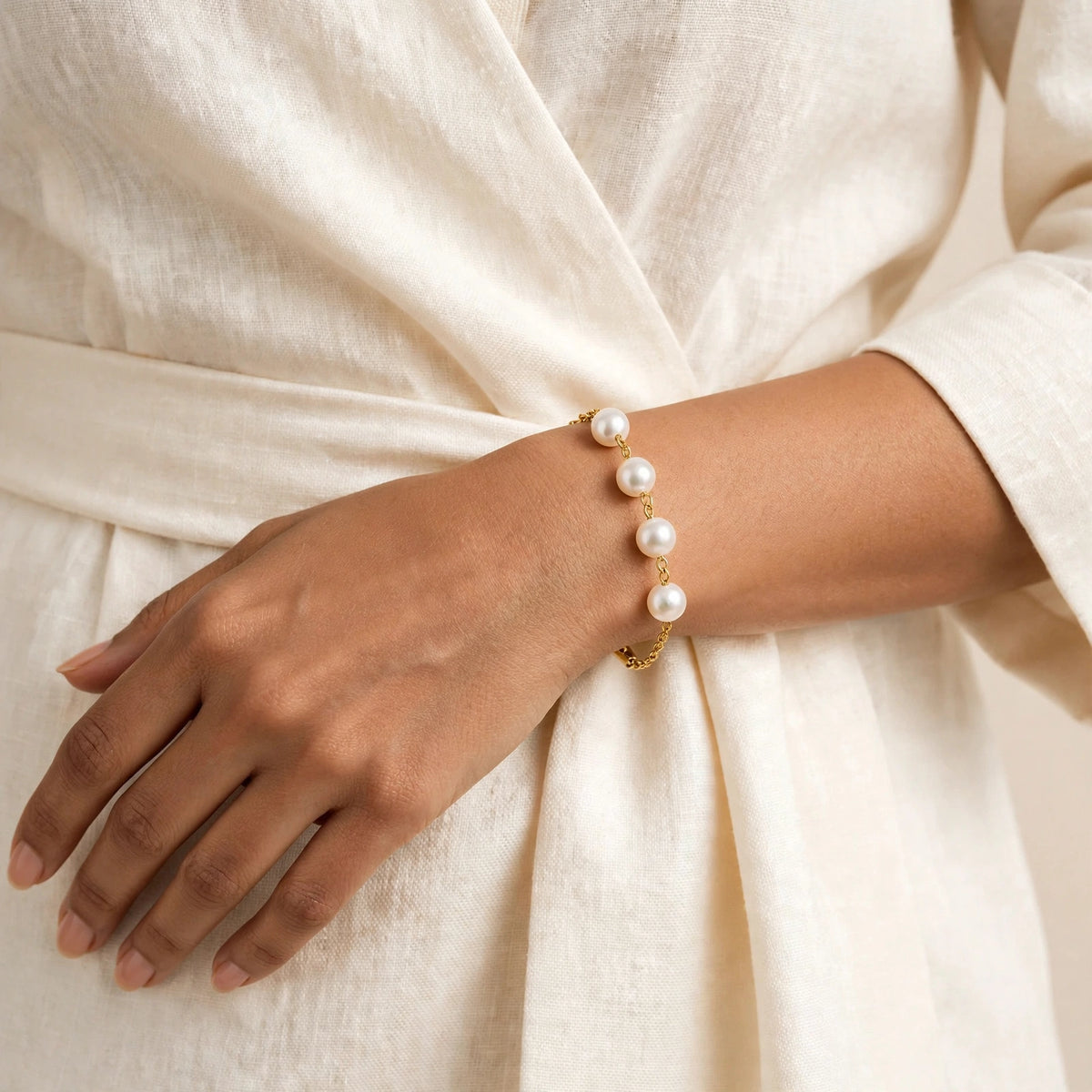 Indian woman's wrist showing only pearl side of gold bamboo bracelet on neutral backdrop