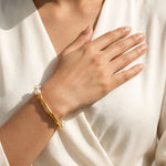 Indian woman's hand on chest wearing single gold bamboo pearl bracelet, close wrist crop