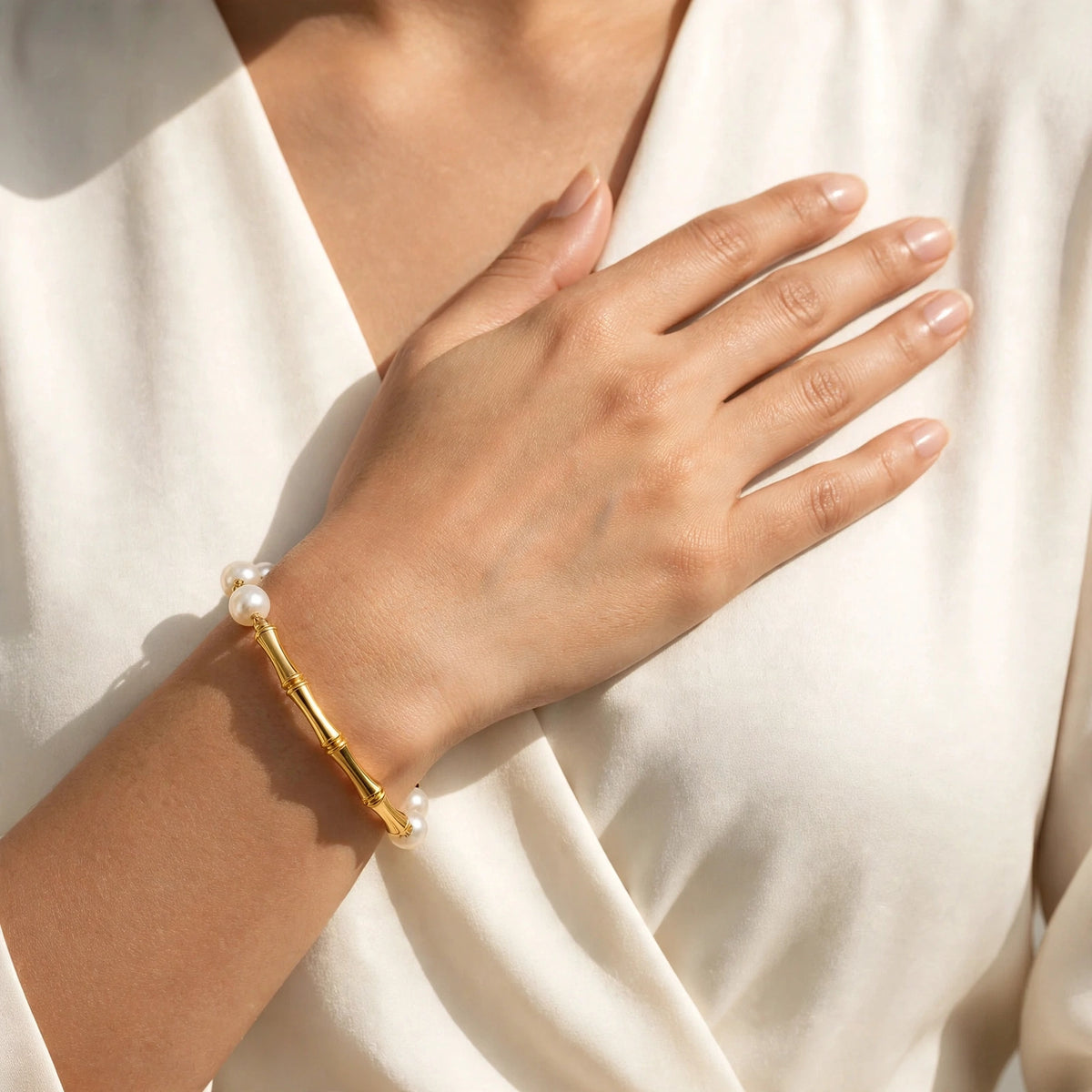 Indian woman's hand on chest wearing single gold bamboo pearl bracelet, close wrist crop