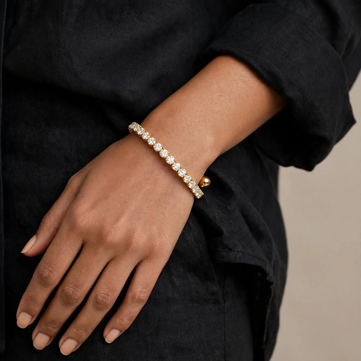 Forearm across waist with gold spiral bracelet, black linen shirt, flawless skin.