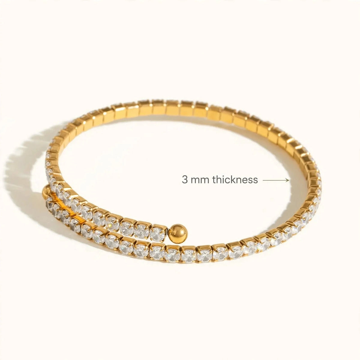 Gold spiral tennis bracelet with 3mm thickness callout on off-white background.