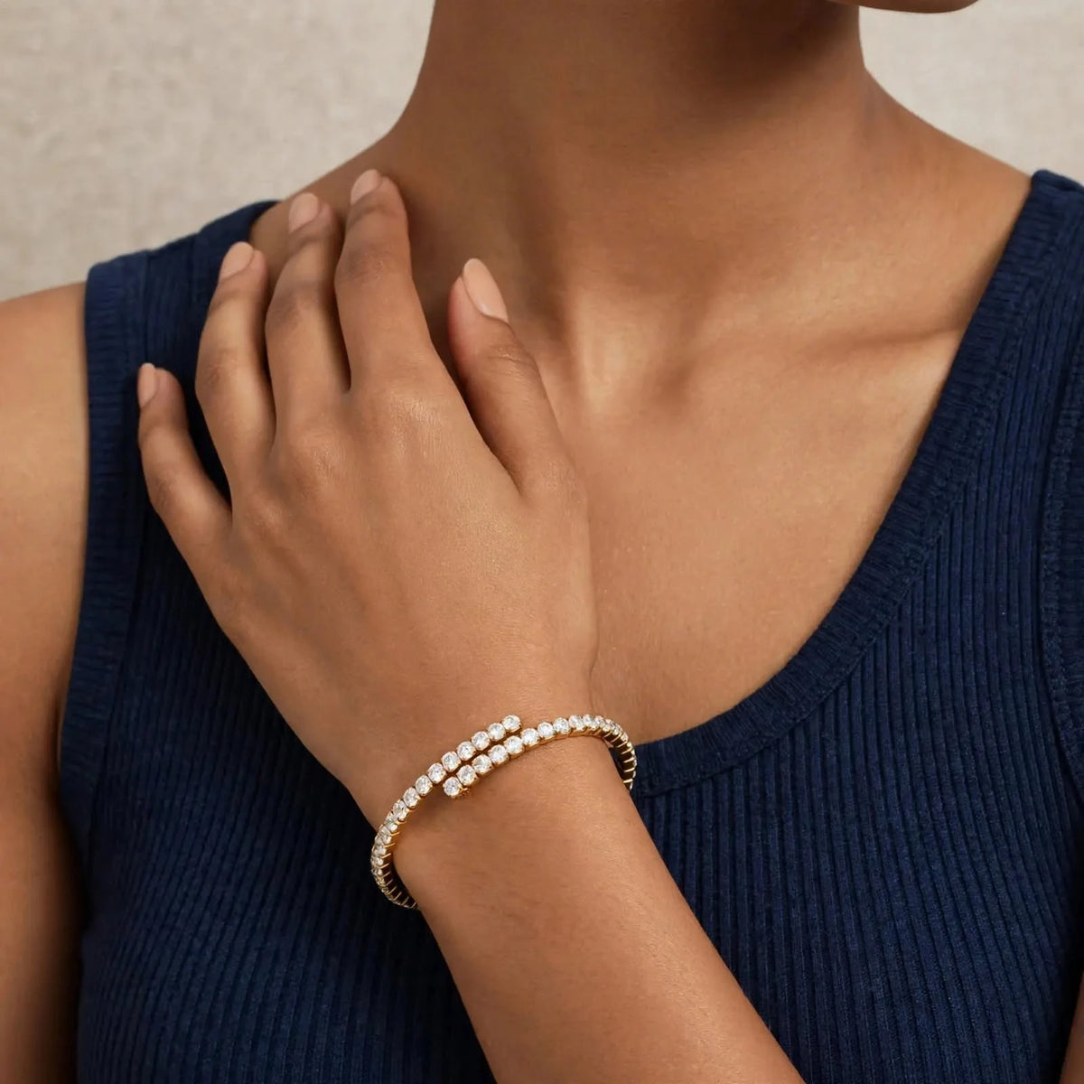 Fingertips at collarbone, gold spiral tennis bracelet single wrap, navy top.