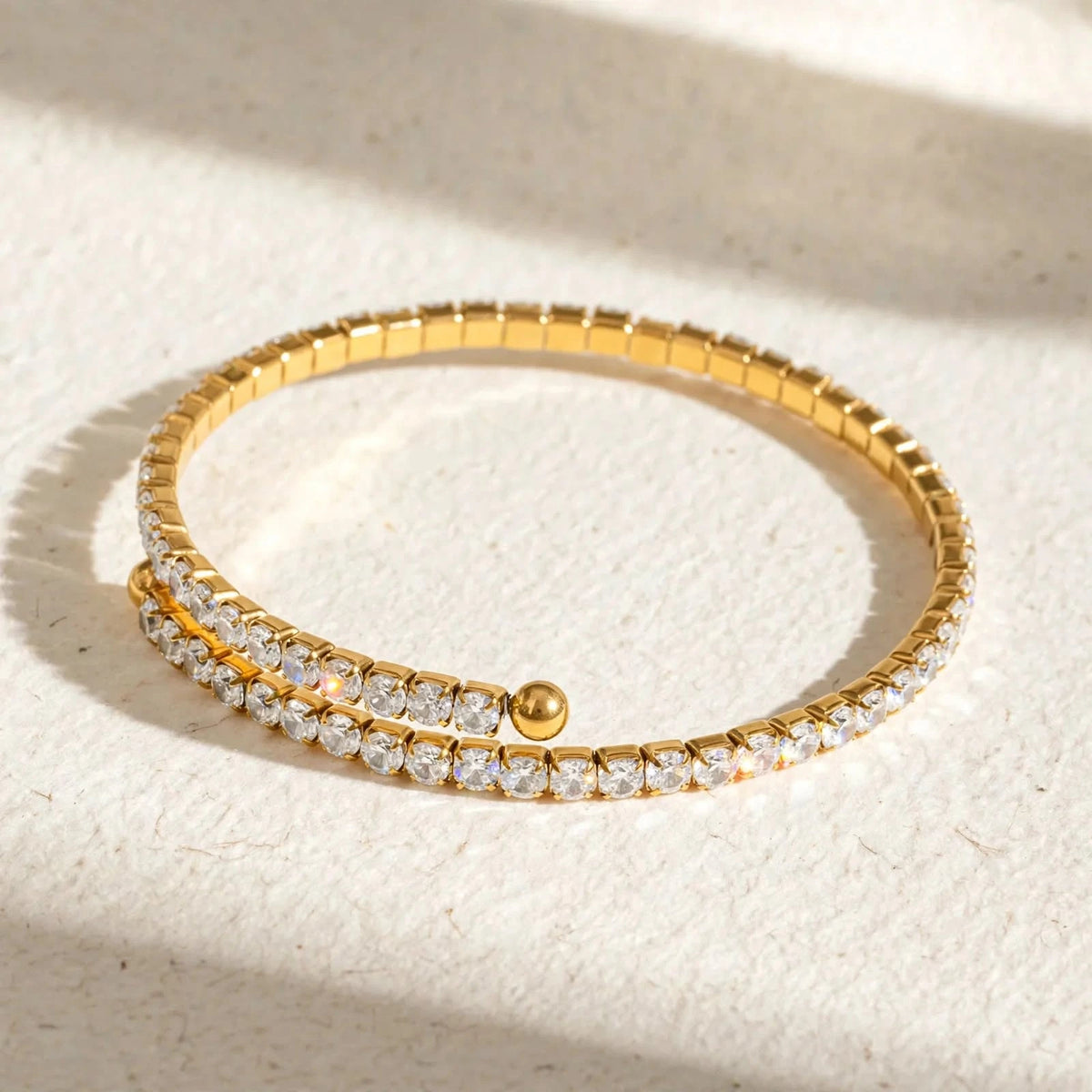 Gold spiral tennis bracelet on textured watercolour paper, window light.