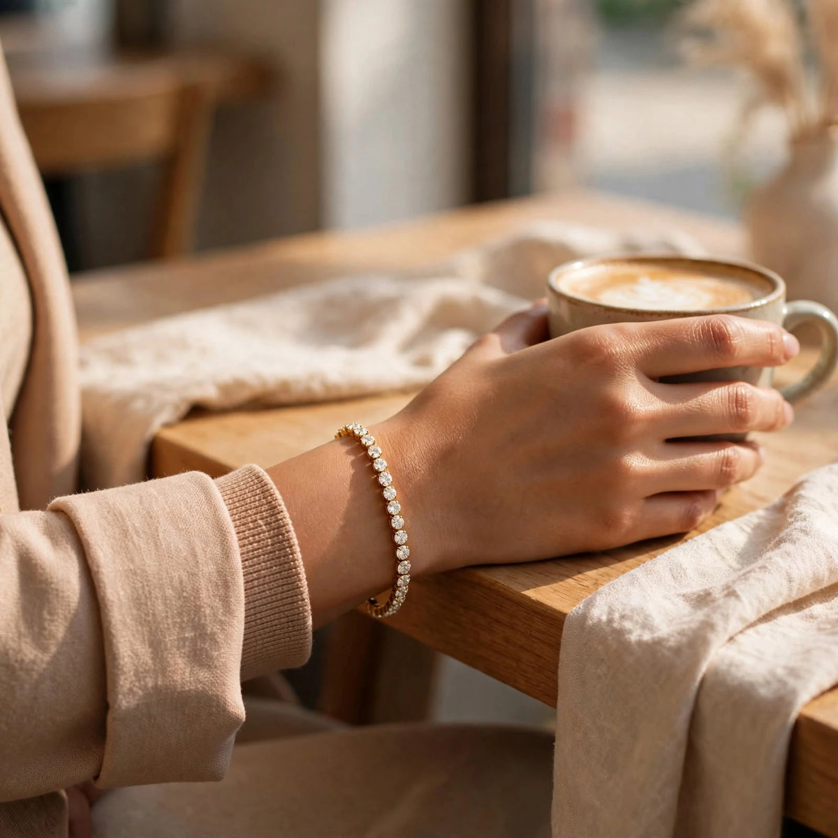 Woman's hand with gold tennis bracelet holding coffee cup on cafe table in sunlight