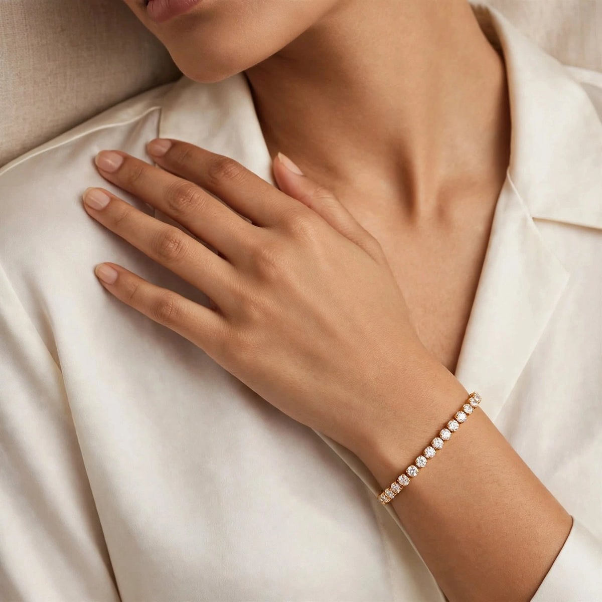 Modern woman in ivory silk blouse, hand on collarbone with gold crystal tennis bracelet.