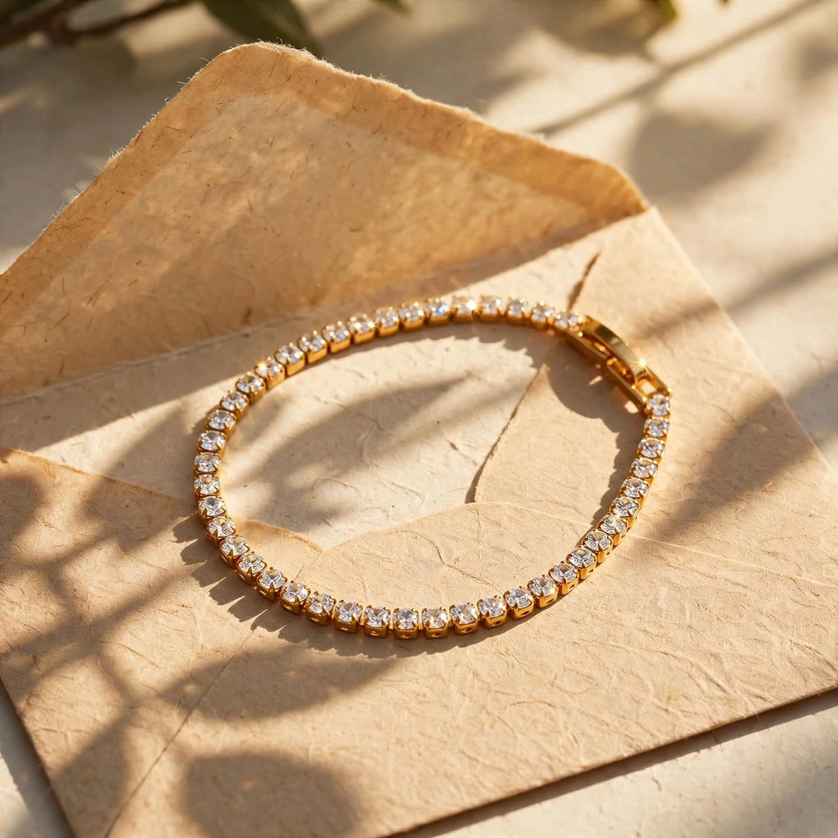 Gold tennis bracelet on handmade paper envelope in warm sun with leaf shadows