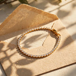 Gold tennis bracelet on handmade paper envelope in warm sun with leaf shadows