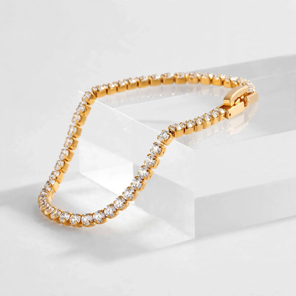 Side view of gold tennis bracelet on clear acrylic riser showing link depth and clasp