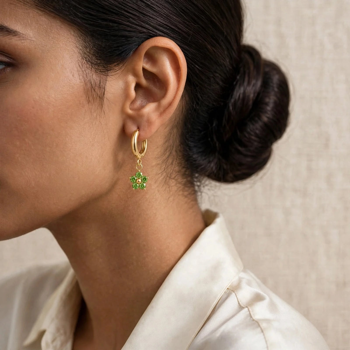 Ear with extra-small green crystal flower huggie charm, ivory silk shirt, low bun