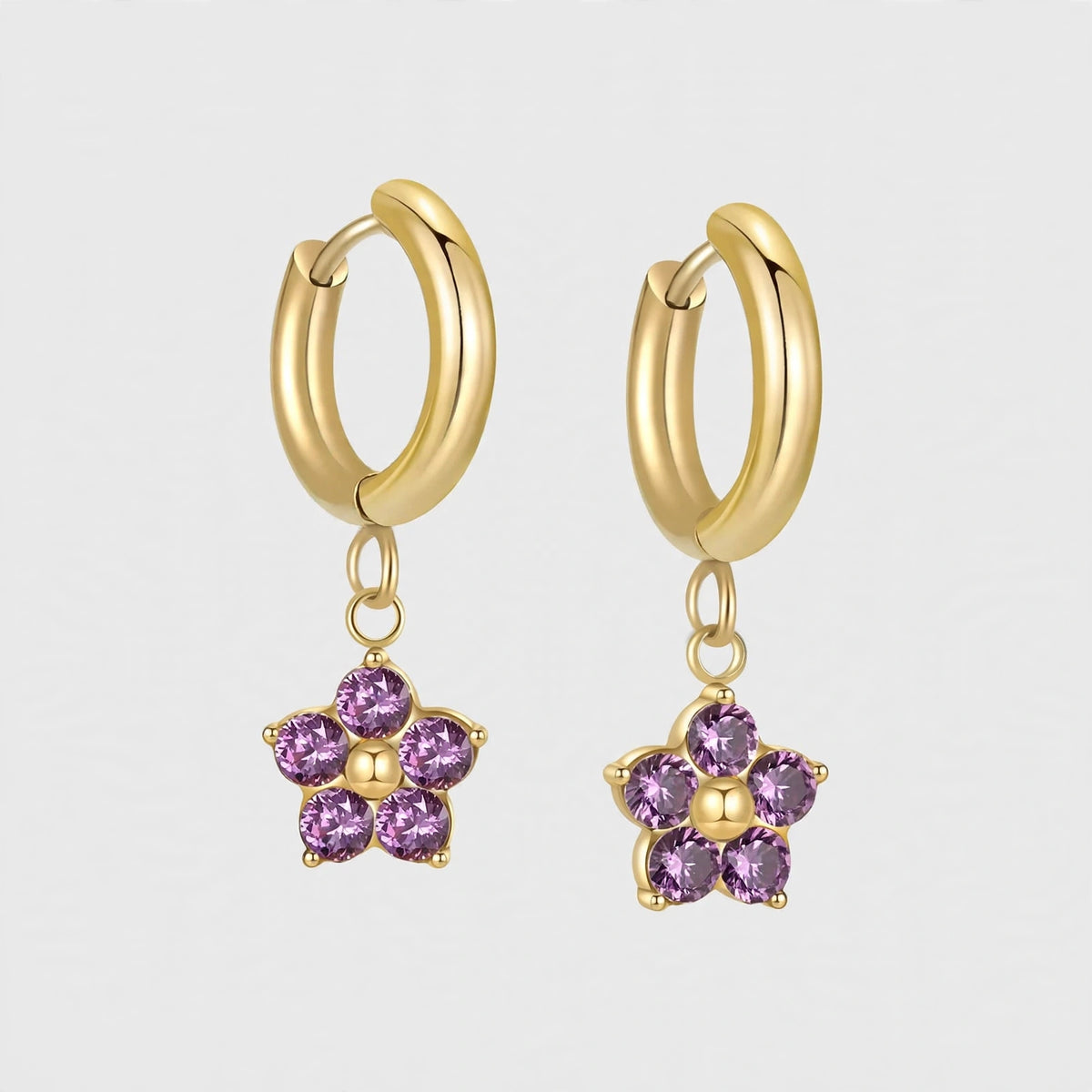 Gold huggie earrings with purple flower charms floating on bright off-white