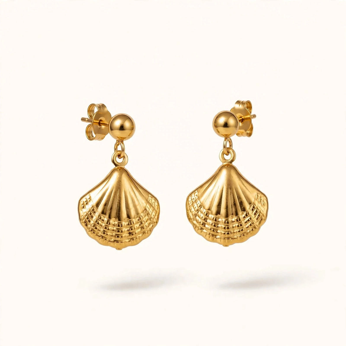 Gold seashell scallop drop earrings with ball stud floating on warm off-white.