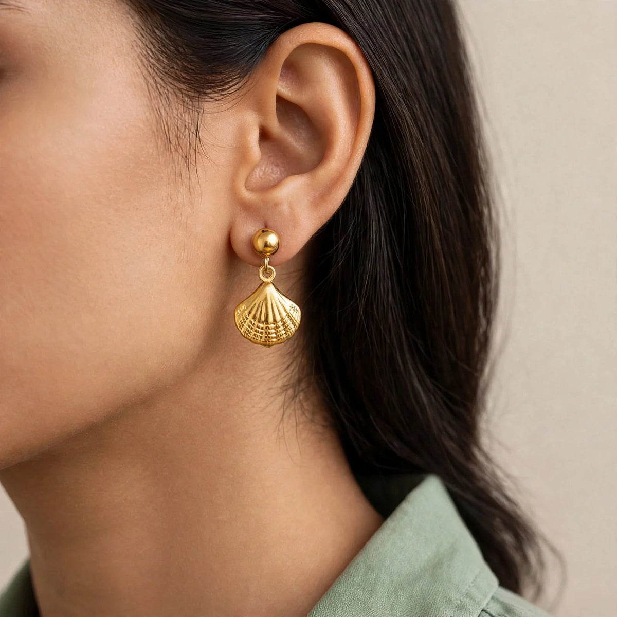 Indian woman profile wearing gold seashell drop earrings with sage shirt, close ear crop.
