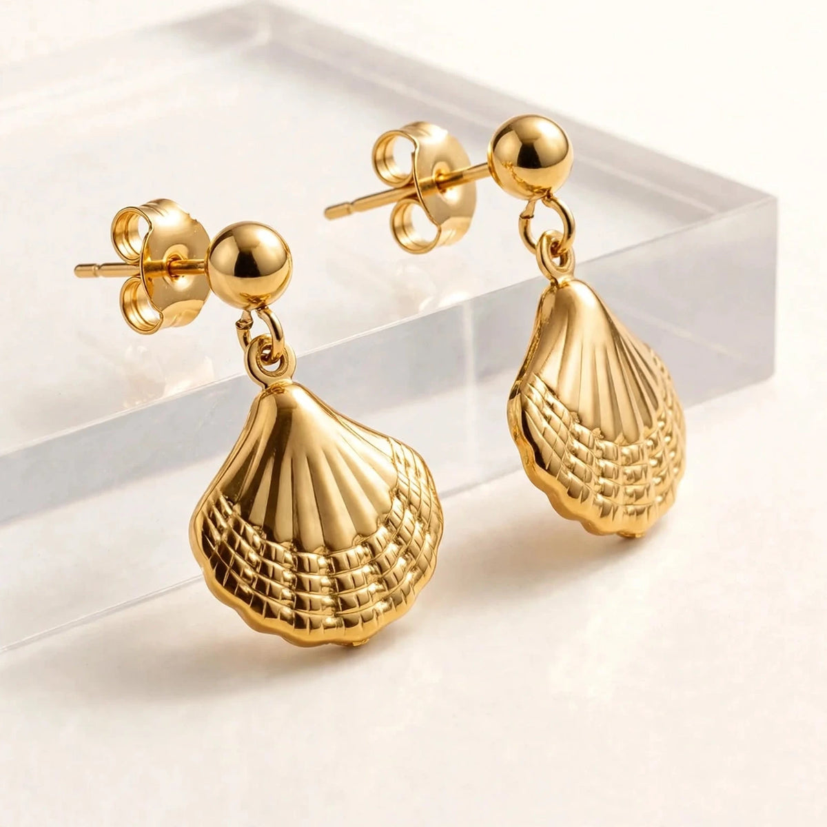 Both gold shell earrings side angle on clear acrylic riser showing depth.