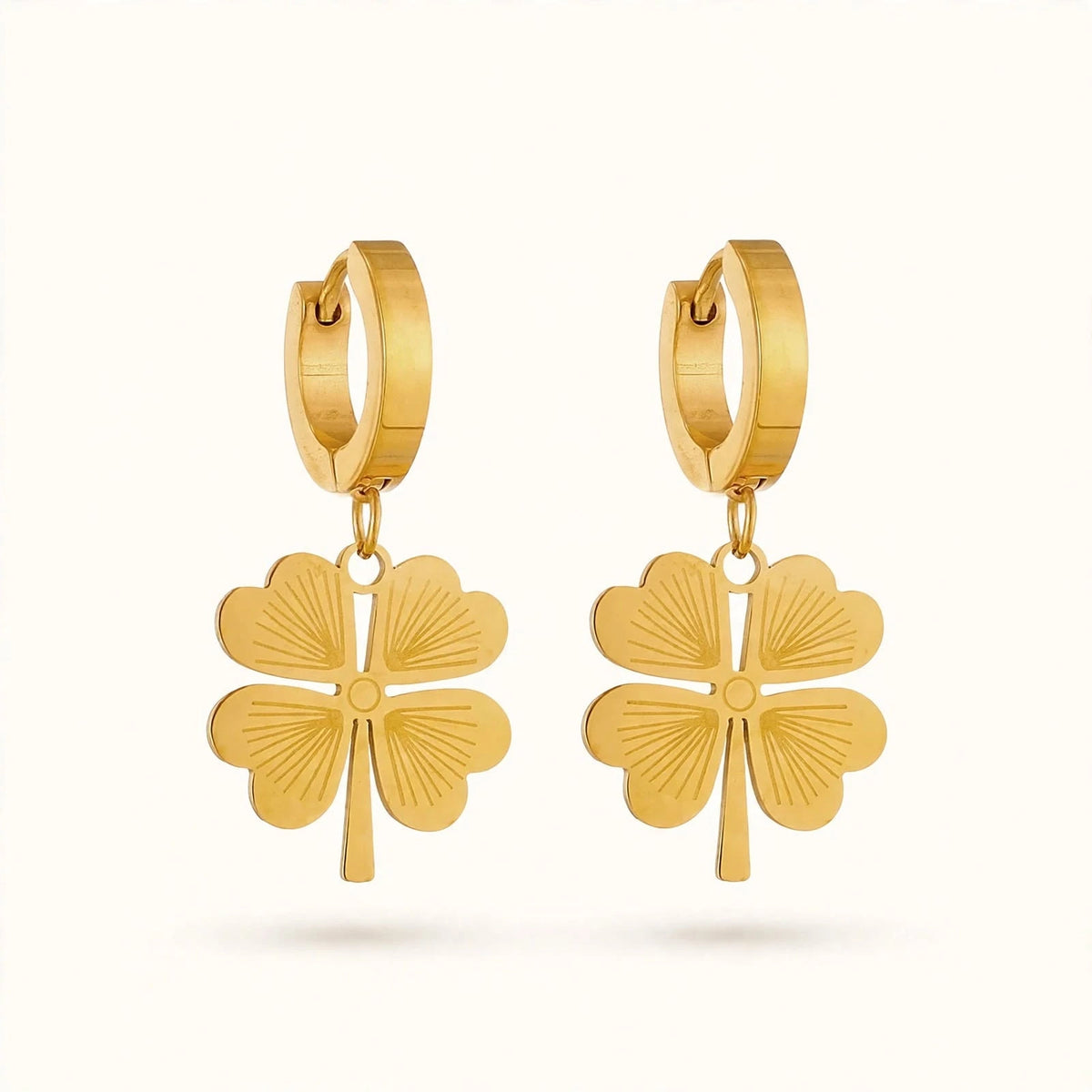 Gold four-leaf clover drop earrings with hinged hoop on off-white background