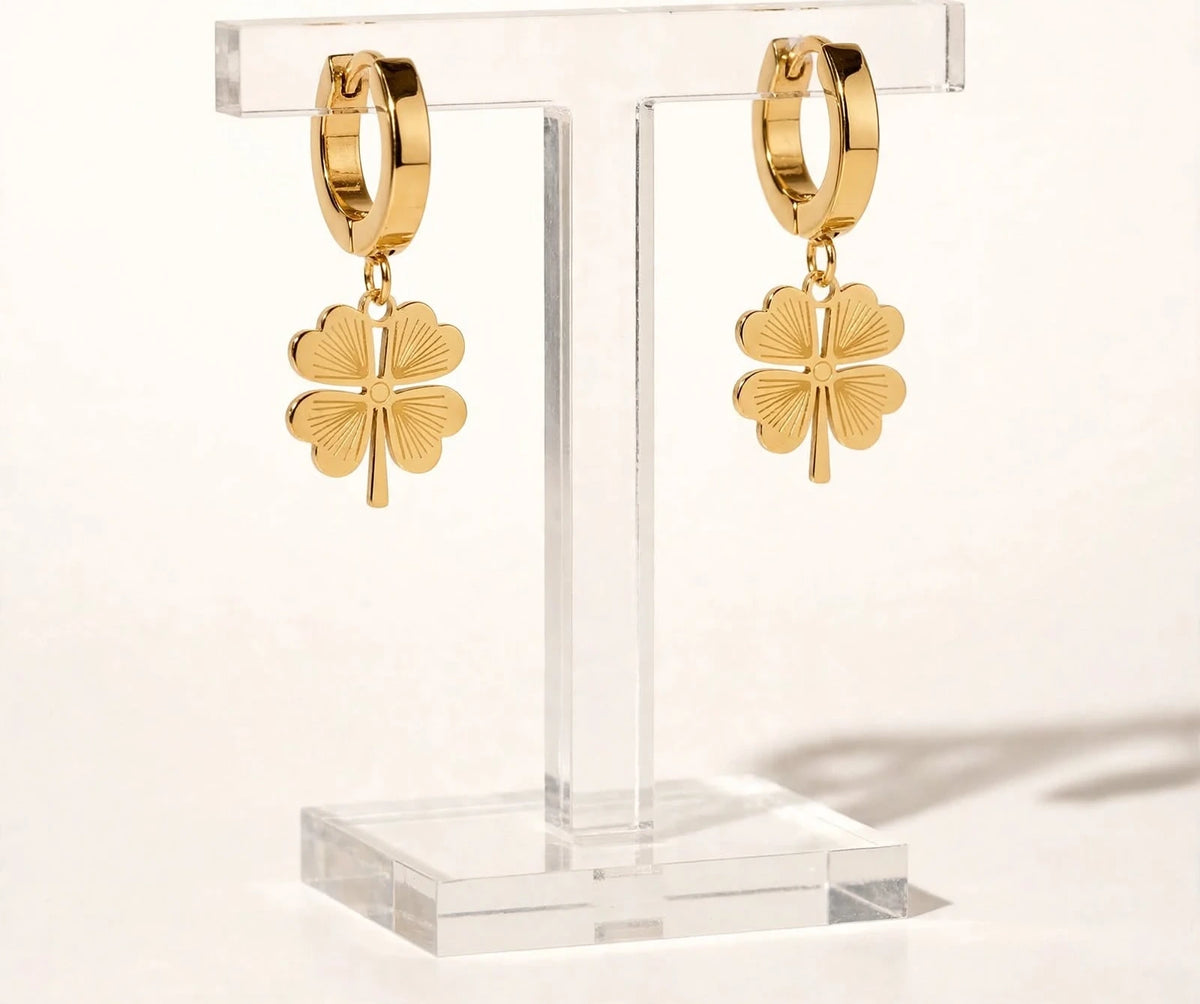 Gold clover drop earrings on clear acrylic stand warm white background