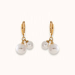 Gold hinged hoop earrings with double white pearl drops on warm off-white background.