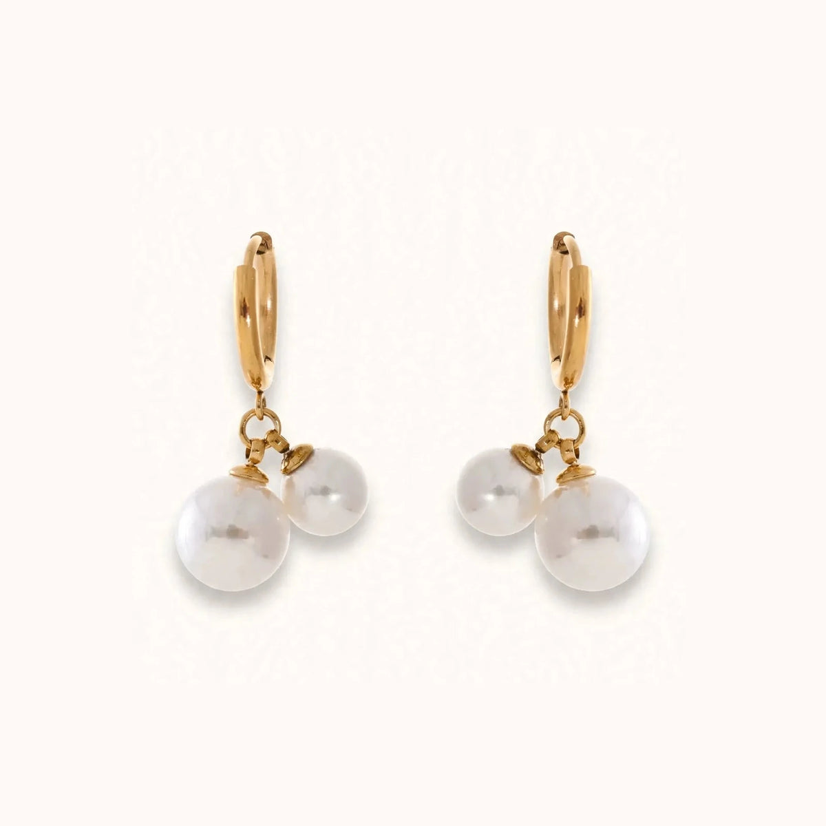 Gold hinged hoop earrings with double white pearl drops on warm off-white background.