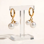Gold huggie hoop double pearl earrings on clear acrylic stand, warm white backdrop