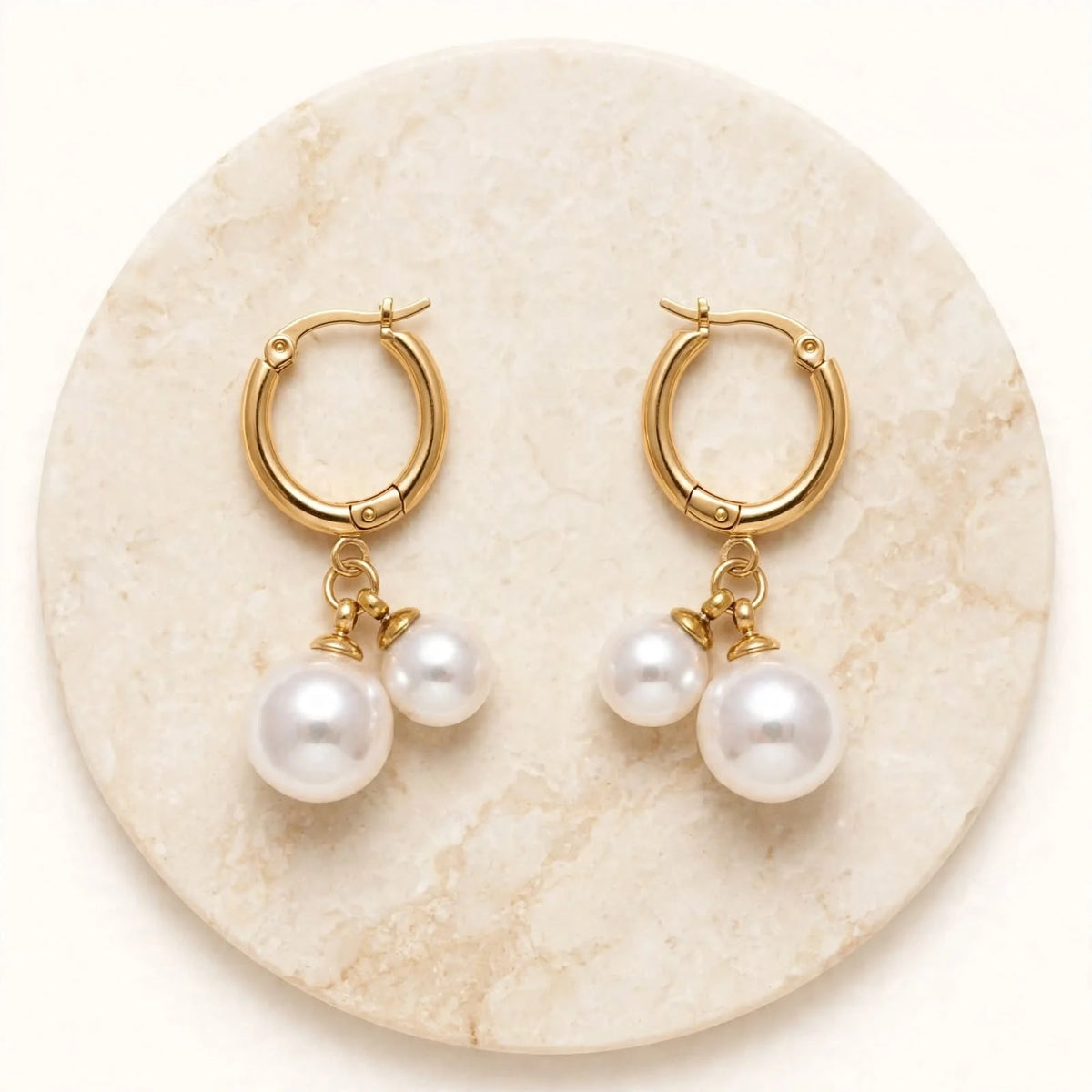 Gold double pearl hoop earrings top view on round cream marble stone