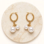 Gold double pearl hoop earrings top view on round cream marble stone