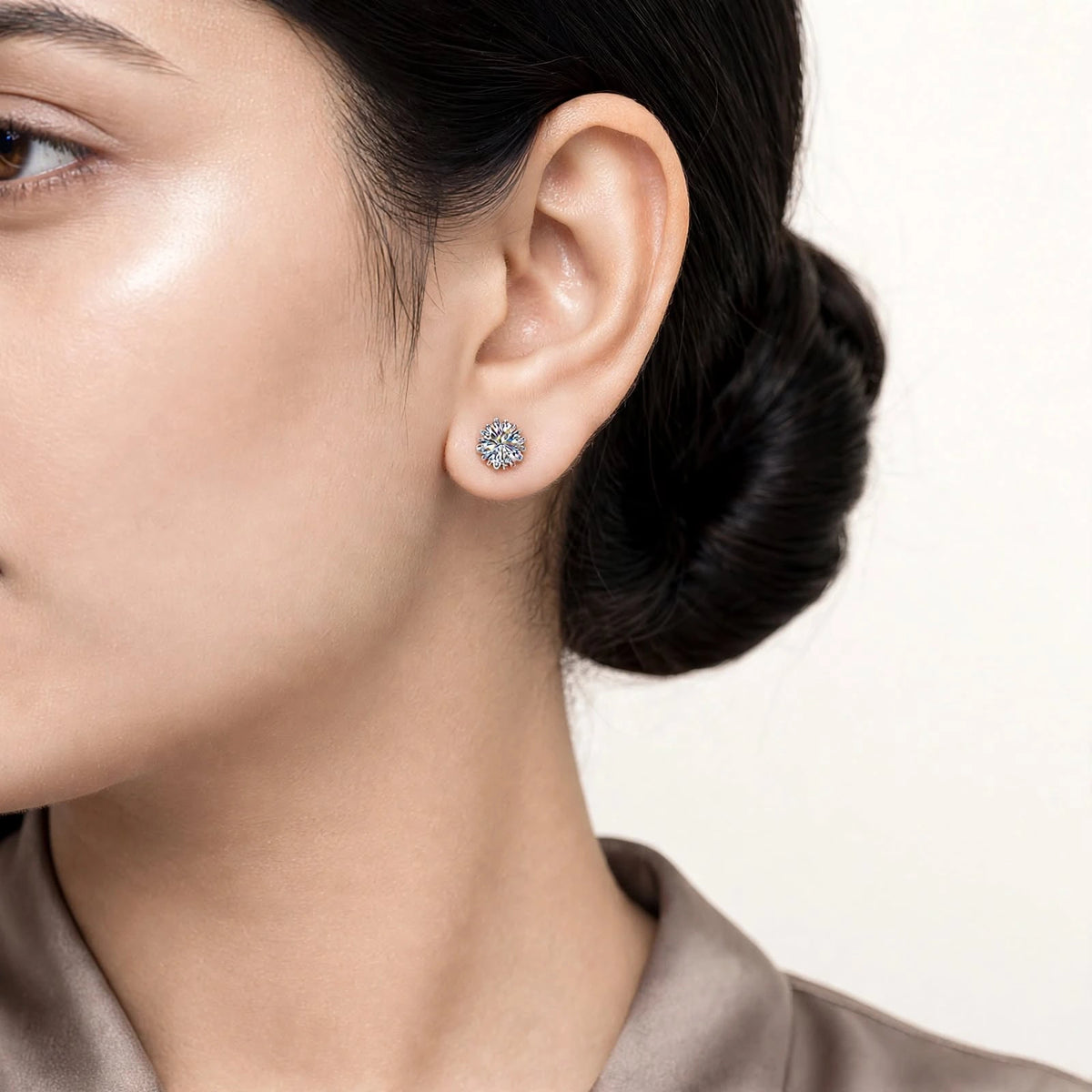 Modern fair skin model sleek bun wearing small 6-prong diamond studs taupe blouse.