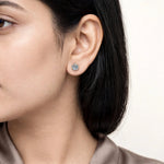 Modern fair skin model wearing small 6-prong diamond studs taupe blouse.