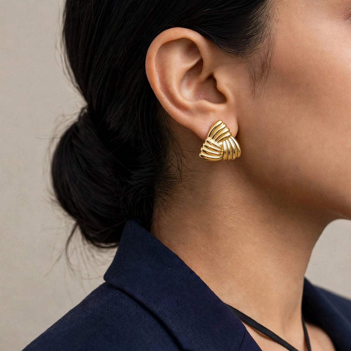 Indian woman in navy blazer over camisole looking over shoulder wearing gold ribbed triangle earrings.
