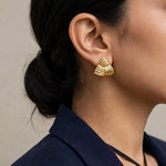 Indian woman in navy blazer over camisole looking over shoulder wearing gold ribbed triangle earrings.
