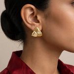 Indian woman in deep red silk shirt with hair tucked, wearing gold triangular ribbed earrings in profile.