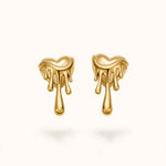 Gold melting heart drip earrings pair floating on warm off-white background.