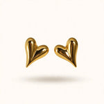 Gold puffed heart stud earrings floating on warm off-white background