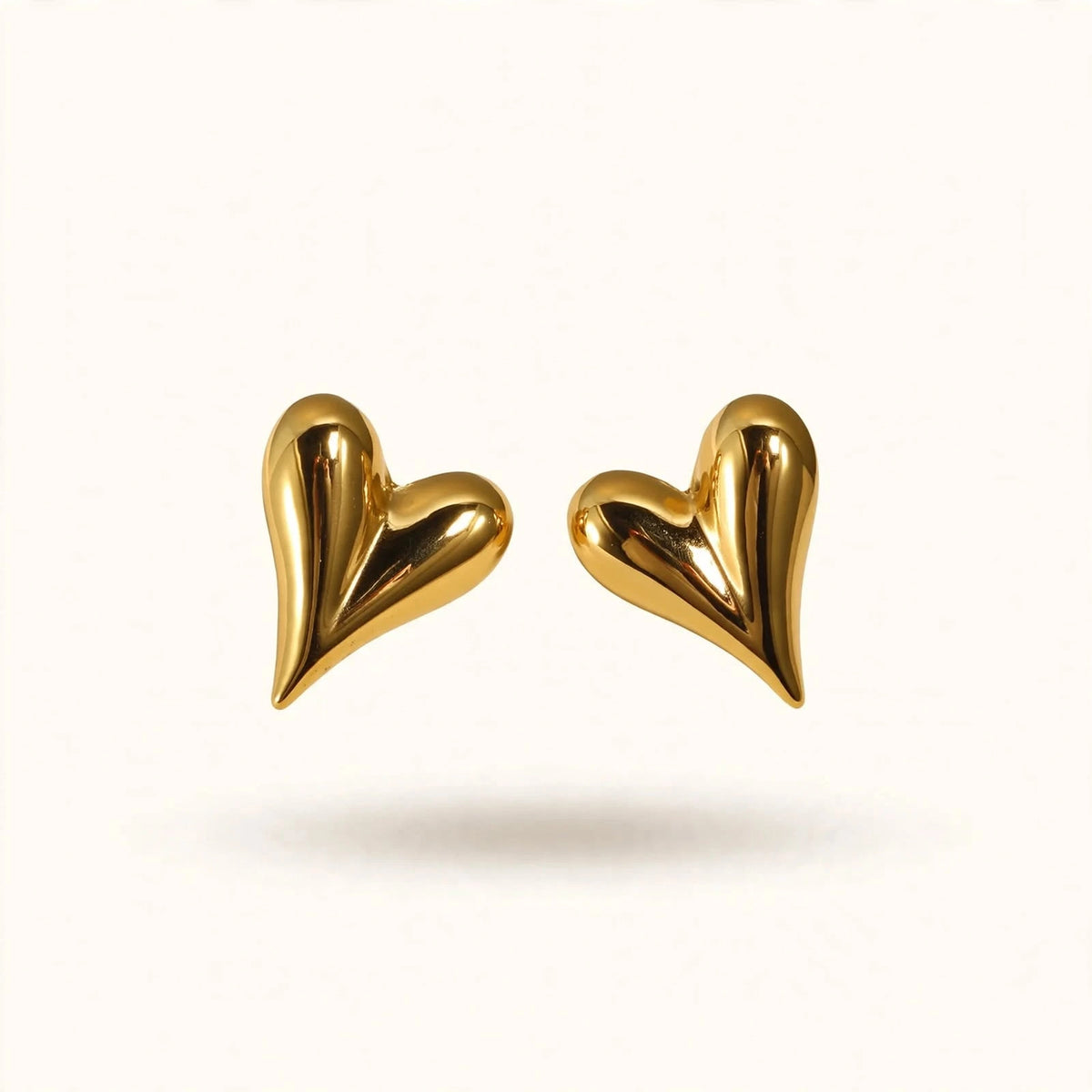 Gold puffed heart stud earrings floating on warm off-white background